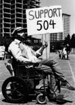 Old photo of a person with a disability holding up a sign reading Support 504.