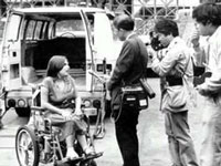 Old photo of a person with a disability talking to news reporters.