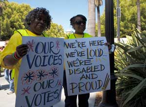 Photo of 2 people holding up disability voting signs.